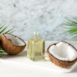 Coconut oil in a clear bottle with half an open coconut fruit on each side.