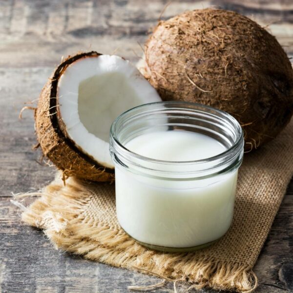 Coconut mil inside a glass jar beside many coconuts