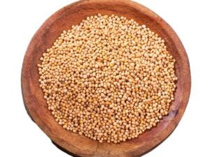 Yellow mustard seeds in a brown bowl.