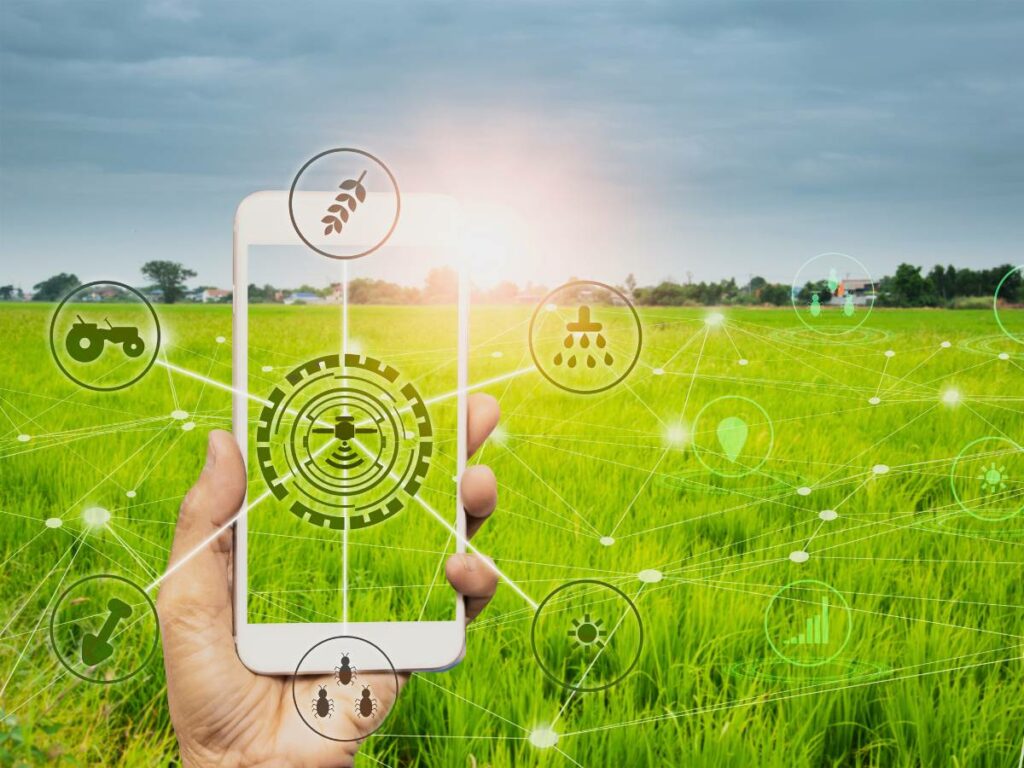 Hand holding a smart phone with agriculture icons on the screen stock foto with a farm in the background.