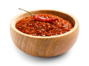 Red chilis flakes in a wooden bowl, garnished by a red chili pepper.
