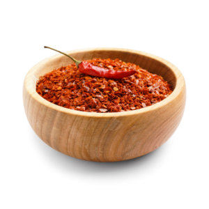 Red chilis flakes in a wooden bowl, garnished by a red chili pepper.