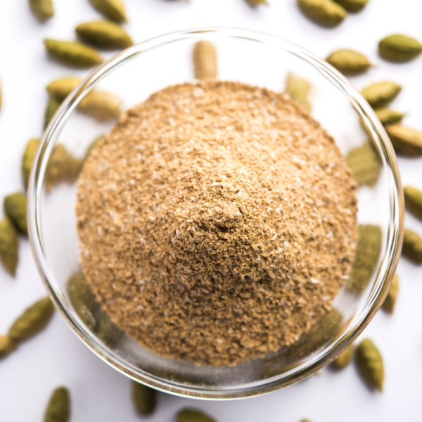 Brown powder in a transparent bowl surrounded by cardamom seeds.