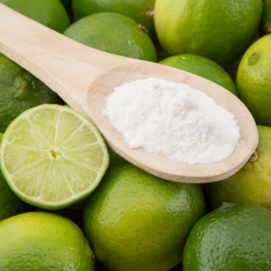 Wooden spoon with white powder on it laying on top of a bed of green lime fruit.