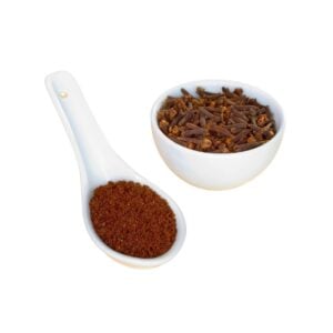 Cloves in a bowl beside a spoon with a heap of reddish-brown powder