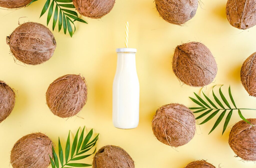 coconut milk in a bottle surrounded by coconuts on a yellow background