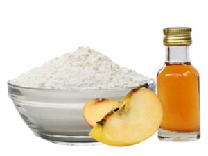 White powder in a transparent bowl, beside a bottle of apple cider and apple slices.