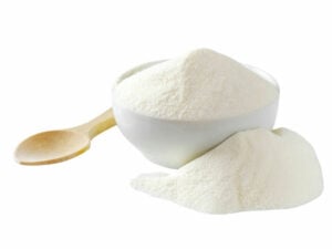 White powder in a bowl beside a heap of white powder and a wooden spoon.