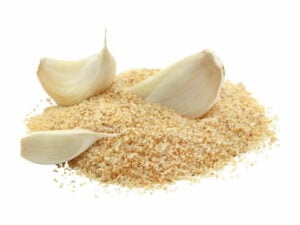 Yellowish brown powder in a heap displayed with three garlic cloves.