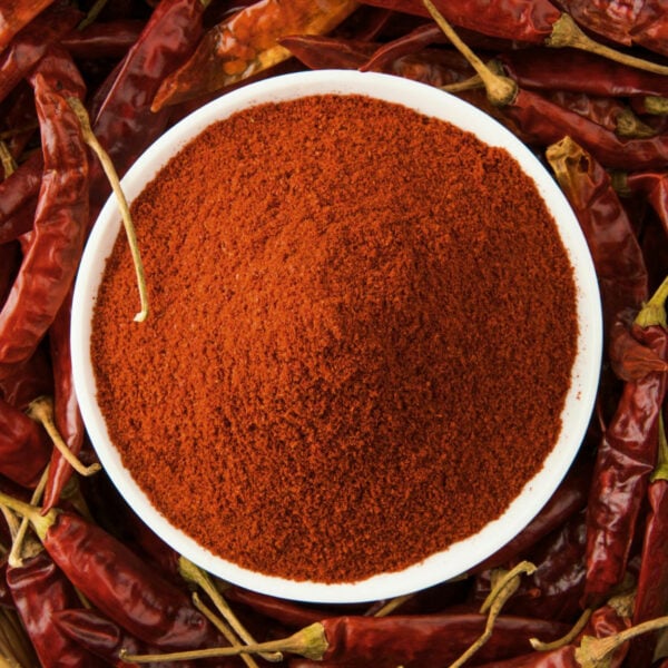 Top view of red powder in a bowl, surrounded by red chili peppers.