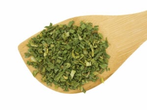 Green, dried herbs on a wooden spoon.